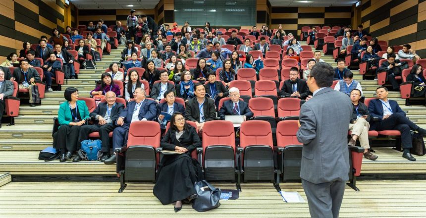 Professional setting of a business conference with attendees and a presenter in an auditorium.